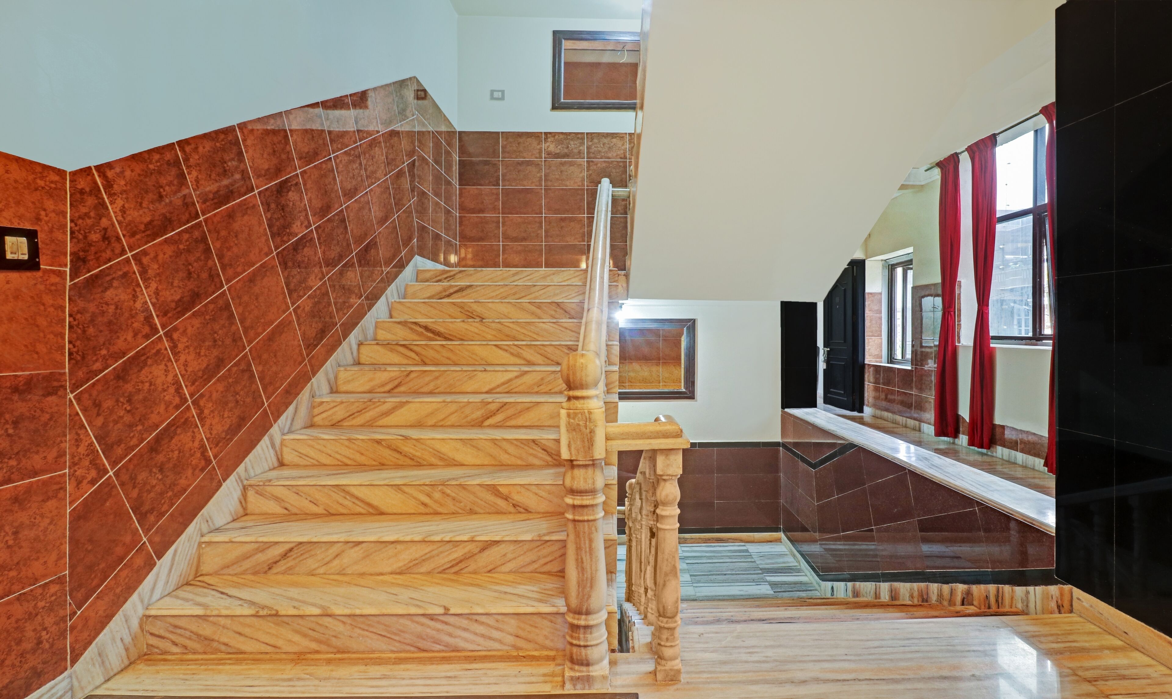 A staircase with wooden steps and a handrail, leading to a landing with a black door and a window with red curtains.