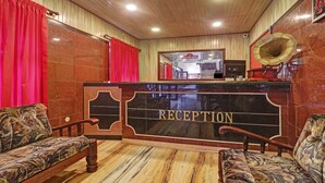 Un área de recepción con piso de mármol, dos sillones estampados, un mostrador de recepción con la palabra 'RECEPTION' escrita en él, y un espejo sobre el mostrador.