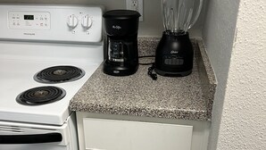 Une cuisine avec un fourneau blanc, une machine à café, un mixeur et une bouilloire rangée dans un placard.