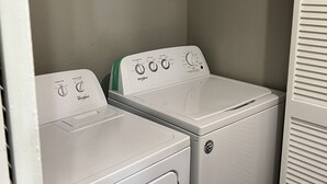Une buanderie équipée de deux lave-linge Whirlpool à chargement frontal et d’une étagère métallique placée au-dessus.