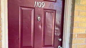 Une porte de couleur bordeaux portant le numéro 1109, une poignée de porte en métal et un heurtoir.