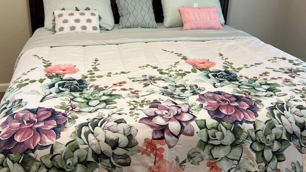 Un lit avec une couvre-lit à motifs floraux, une tête de lit sombre et trois oreillers aux motifs différents.