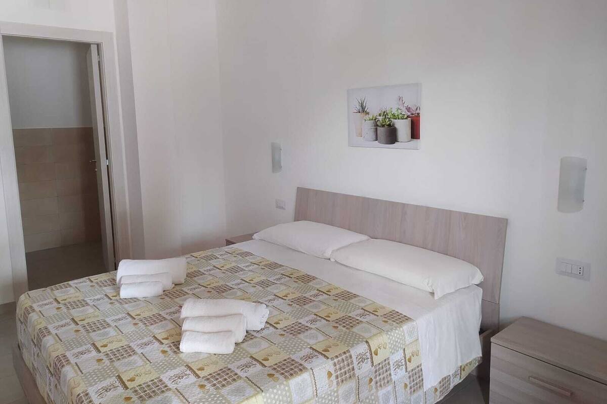 A bedroom with a bed, a nightstand, a wall-mounted shelf with plants, and a door leading to a bathroom.