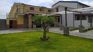 Una casa de dos plantas con un balcón, un porche cubierto y un pequeño jardín con un árbol.