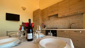 Una mesa de comedor dispuesta con platos blancos, copas de vino y una botella de vino, con armarios de madera y un salpicadero de azulejos al fondo.