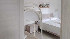 Un dormitorio minimalista con una cama individual sobre otra, una mesita de noche y un estante en la pared con plantas.