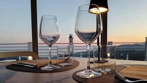Mesa servida con dos copas de vino, una vela y un tenedor en una terraza con vistas al atardecer.