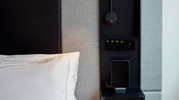 A modern bedroom with a large bed, a wall-mounted lamp, and a built-in shelf with a tablet.