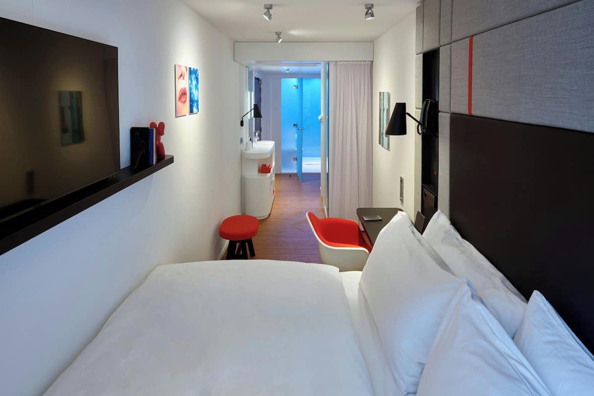 A hotel room with a large bed, a small desk, a chair, and a bathroom visible through an open door.