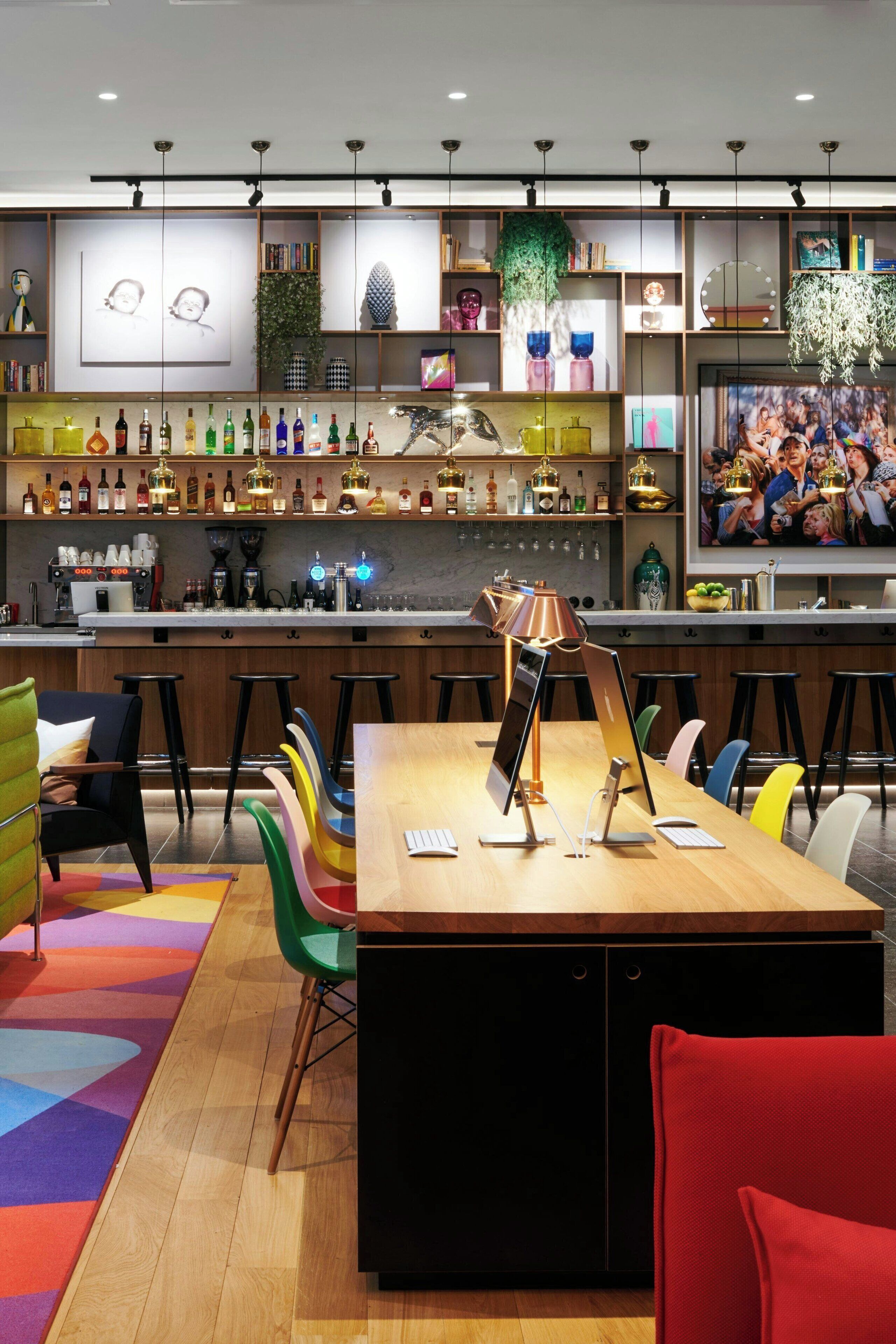 A modern bar area with a wooden bar counter, stools, and a variety of bottles.