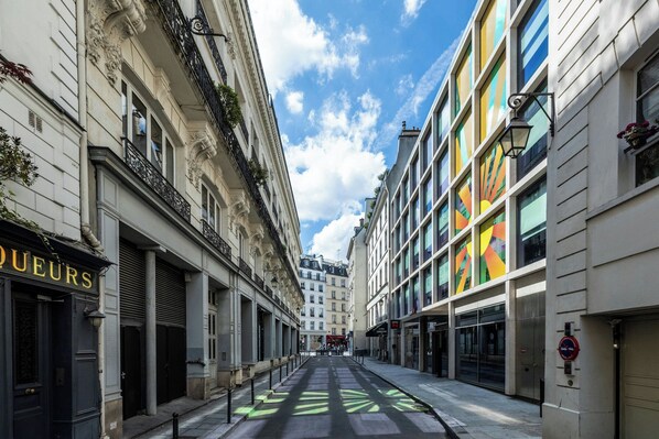 A street with buildings, including a shop with 'QUEURS' sign, and a colorful building with a geometric pattern.