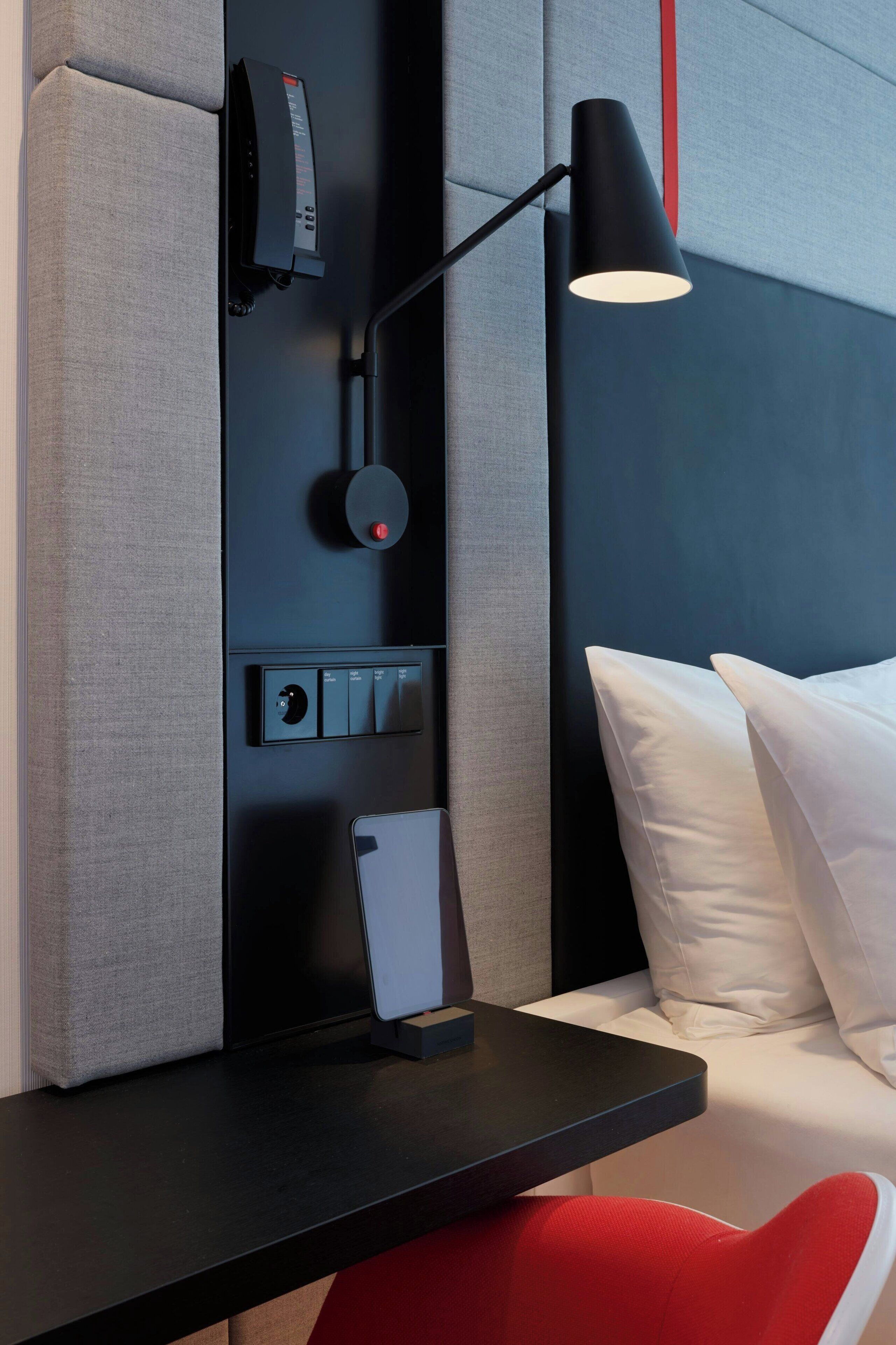 A modern room with a black desk, a red chair, a white pillow, and a black lamp.