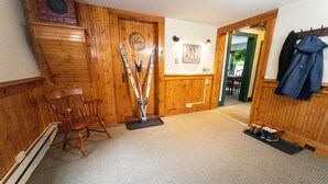 Un interior de madera con una silla, esquíes apoyados en una pared y un perchero con una chaqueta.