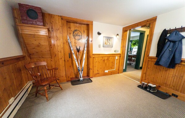 A wooden interior with a chair, skis leaning against a wall, and a coat rack with a jacket.