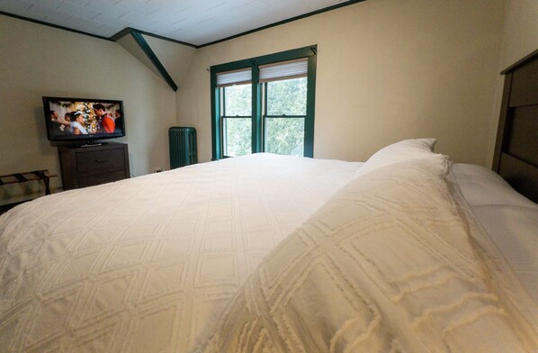 Un dormitorio con una cama grande, un televisor en una cómoda y una ventana con persianas.