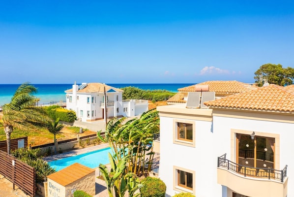 A coastal residential area with a swimming pool, white buildings, and a clear view of the sea.