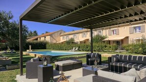 Une terrasse extérieure avec des meubles en osier, une piscine et un espace abrité.