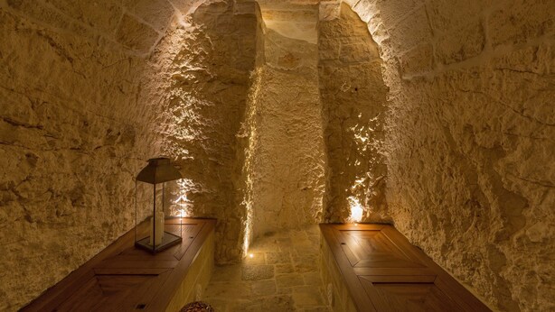 Un intérieur aux murs de pierre, avec un banc en bois et un lampadaire.