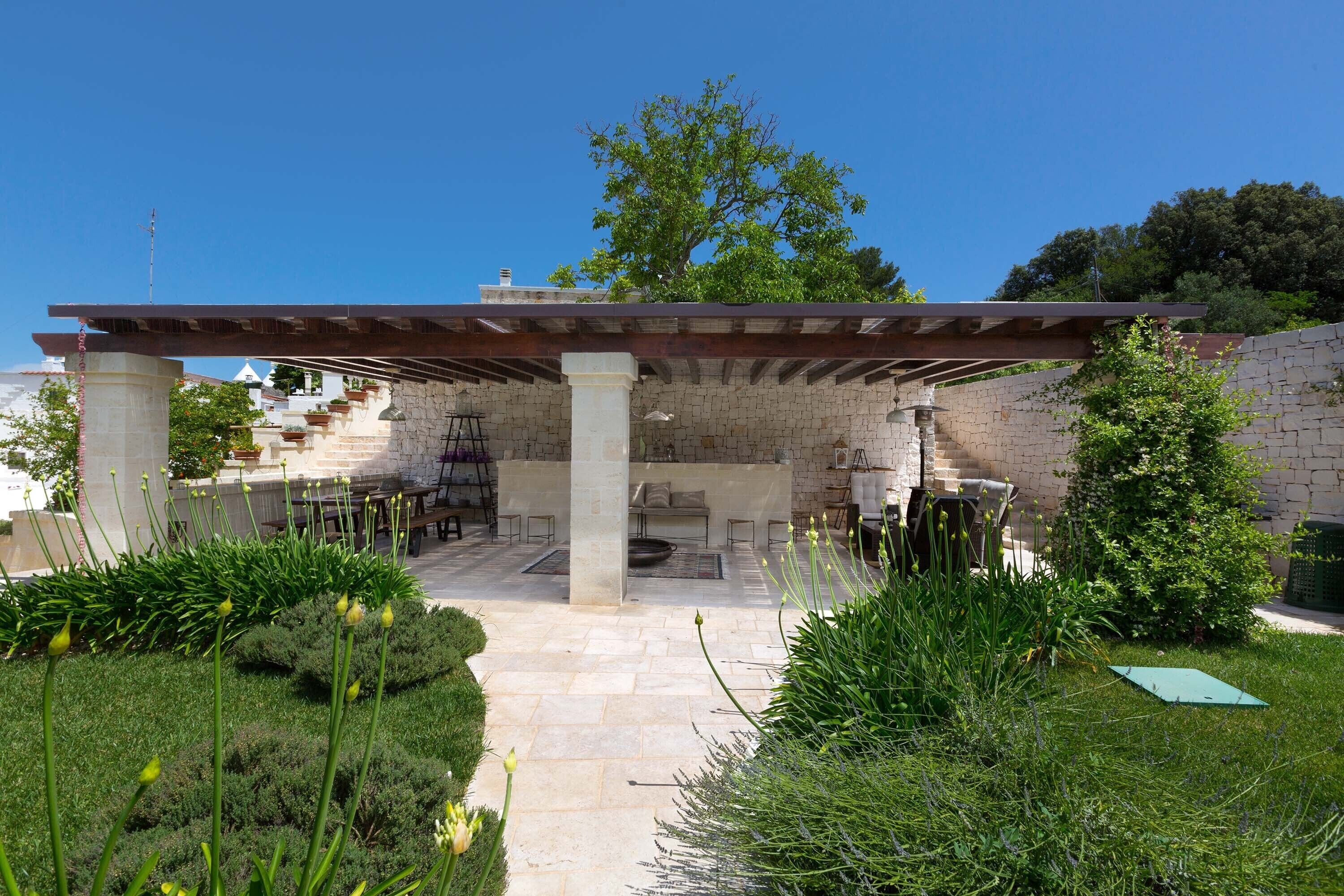 An outdoor patio area with stone flooring, a pergola, and a stone wall.