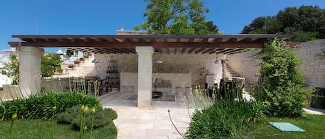 An outdoor patio area with stone flooring, a pergola, and a stone wall.