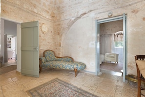 A room with a patterned rug, a blue armchair, and a white chair. - 1970 Trulli Del Monsignore by Perle di Puglia (Fasano)