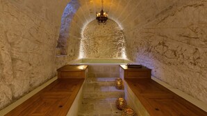 Une pièce aux murs de pierre, avec un banc en bois, une baignoire et un lustre.