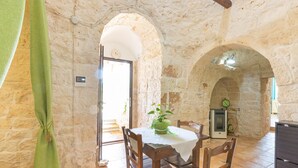 A rustic stone-walled room with a dining table, chairs, and a small heater.