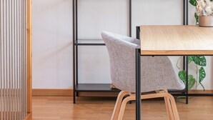 Ein Zimmer mit Holzboden, einer weißen Wand, einem schwarzen Metallregal mit Pflanzen, einem Holztisch und einem Stuhl.