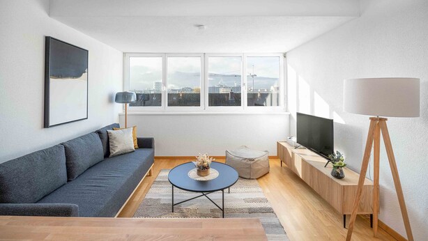 Ein modernes Wohnzimmer mit einer Couch, einem runden Couchtisch, einem Fernseher auf einem Holzständer und einer Stehlampe.