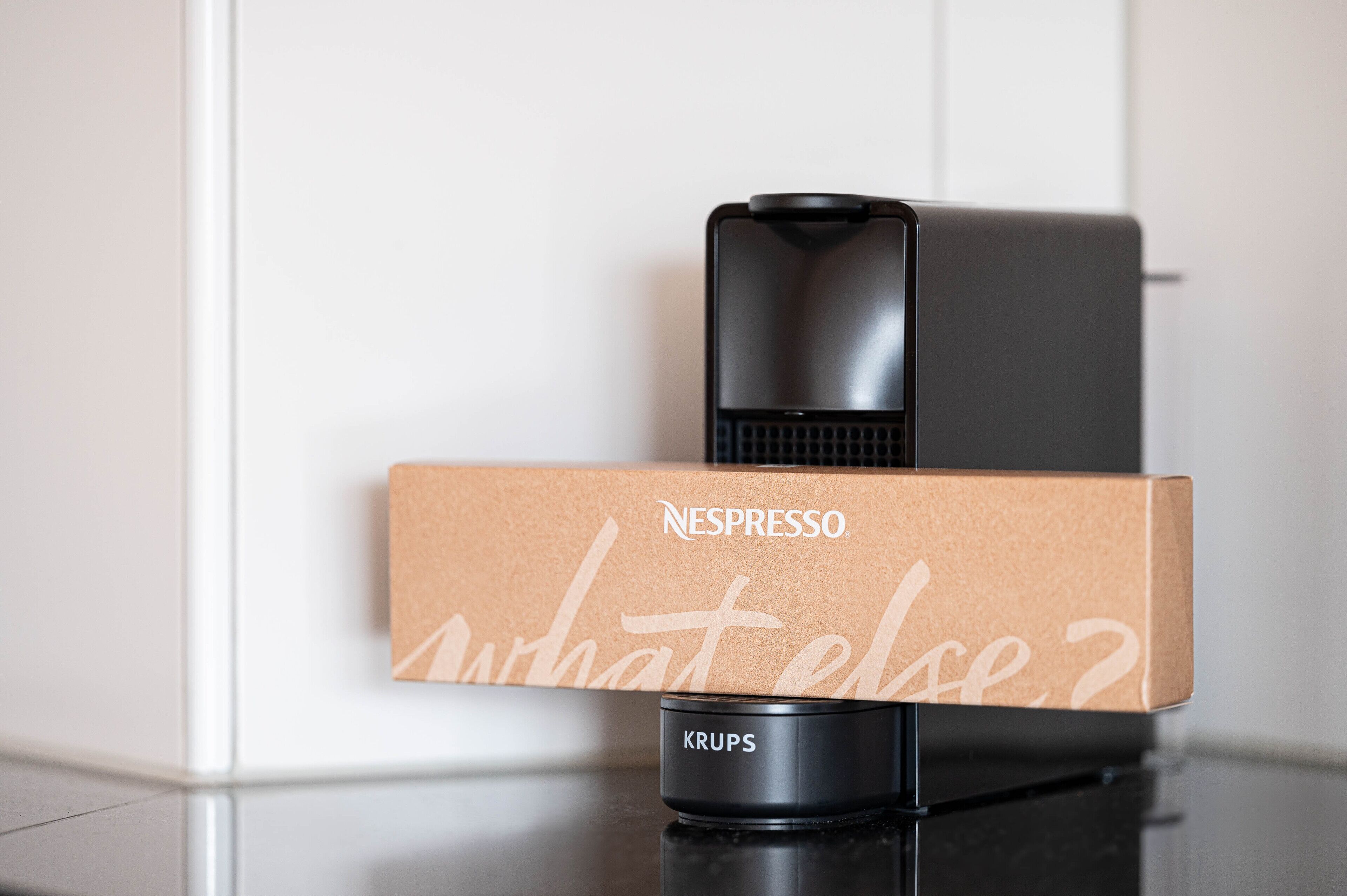 Een Nespresso koffieapparaat en de doos waarin het verpakt zit, staan op een zwart aanrecht.