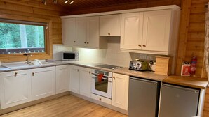 A compact kitchen with white cabinets, a microwave, a toaster, and a refrigerator. - Log cabin with veranda, nestled in Kenwick Park, Louth (Louth)