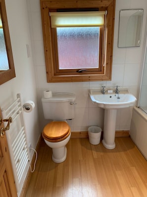 Bathroom features a toilet, pedestal sink, and small window.