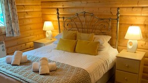 A cozy wooden cabin bedroom with a bed, two bedside tables, and lamps. - Log cabin with veranda, nestled in Kenwick Park, Louth (Louth)