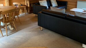 A cozy cabin interior with a wooden dining table, a sofa, and a lamp. - Log cabin with veranda, nestled in Kenwick Park, Louth (Louth)