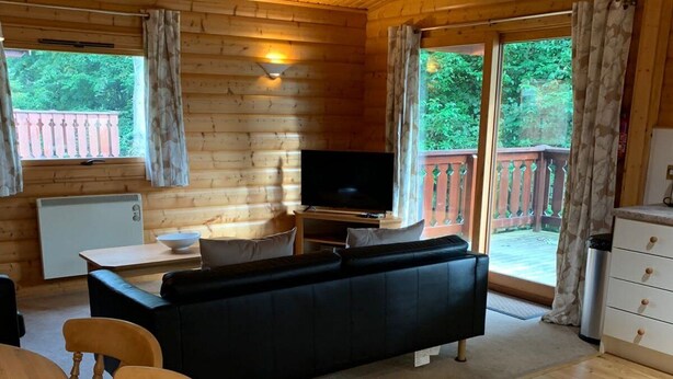 A wooden cabin interior with a sofa, TV, dining table, and chairs. - Log cabin with veranda, nestled in Kenwick Park, Louth (Louth)