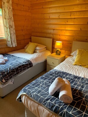 Relax in a warm and inviting room with two beds, a bedside table, and a window with curtains.
