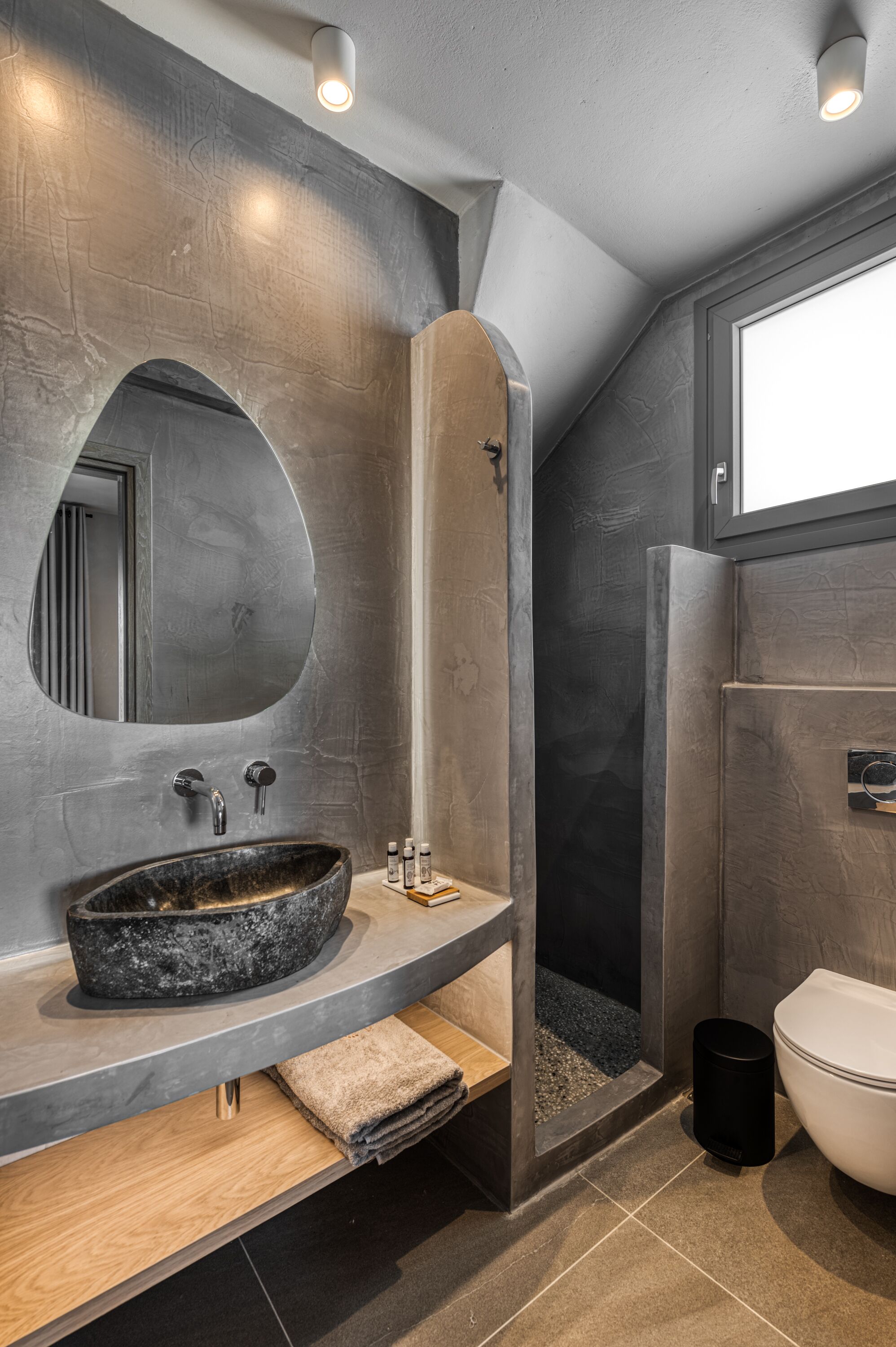 A modern bathroom with a large oval mirror, a round sink, and a shower enclosure.