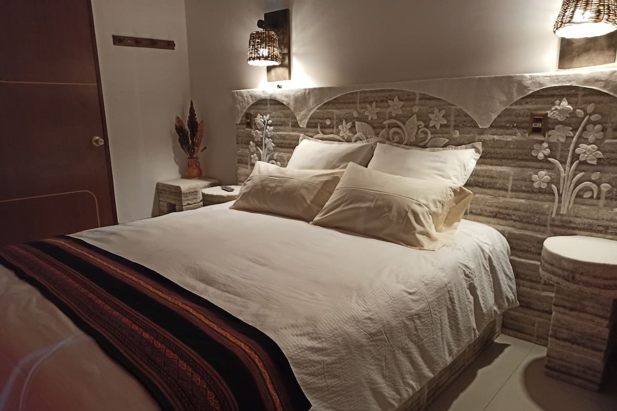 Een opgemaakt bed met een gestreept deken, een nachtkastje met een vaas en een wandlamp.
