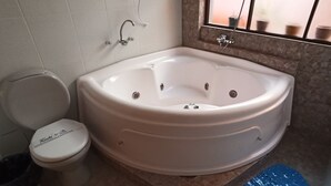 A bathroom with a large bathtub, a toilet, and a window with a view of the outside.