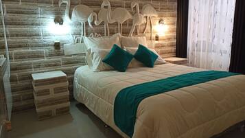 Un dormitorio con cabecera de ladrillo, una cama grande con ropa de cama blanca y almohadas turquesa, una mesita de noche con lámpara y una ventana con cortinas translúcidas.