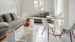 A modern living room with a grey sofa, white chairs, a round table with a laptop, and a vase with flowers. - Akrogiali Beach Hotel Apartments (Hersonissos)