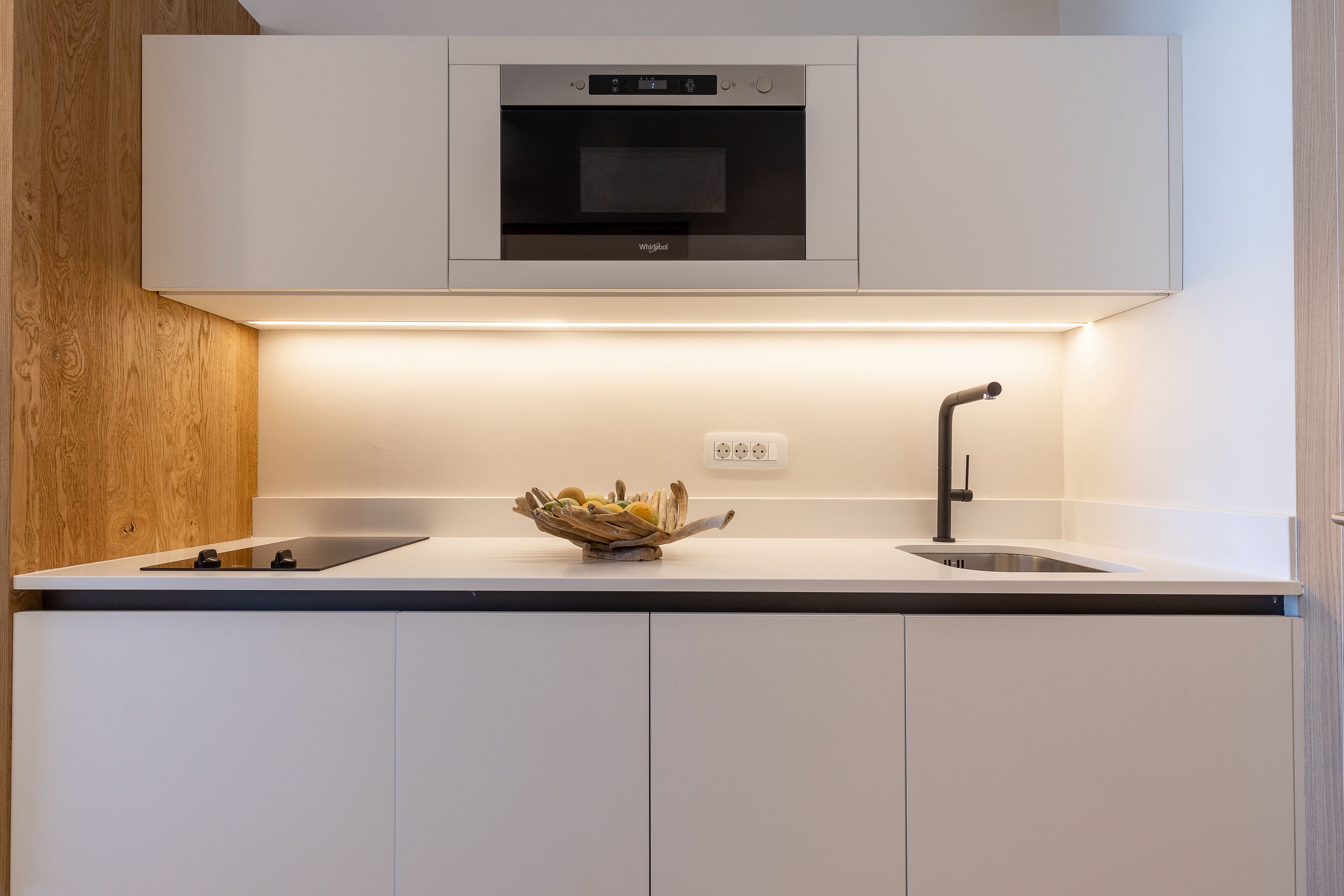 Una cocina moderna con horno integrado, un lavabo y una encimera con un cuenco de fruta.