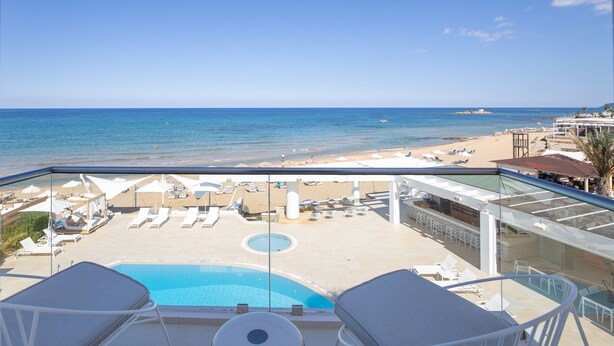 A balcony with a pool, lounge chairs, and a view of the beach and ocean. - Akrogiali Beach Hotel Apartments (Hersonissos)