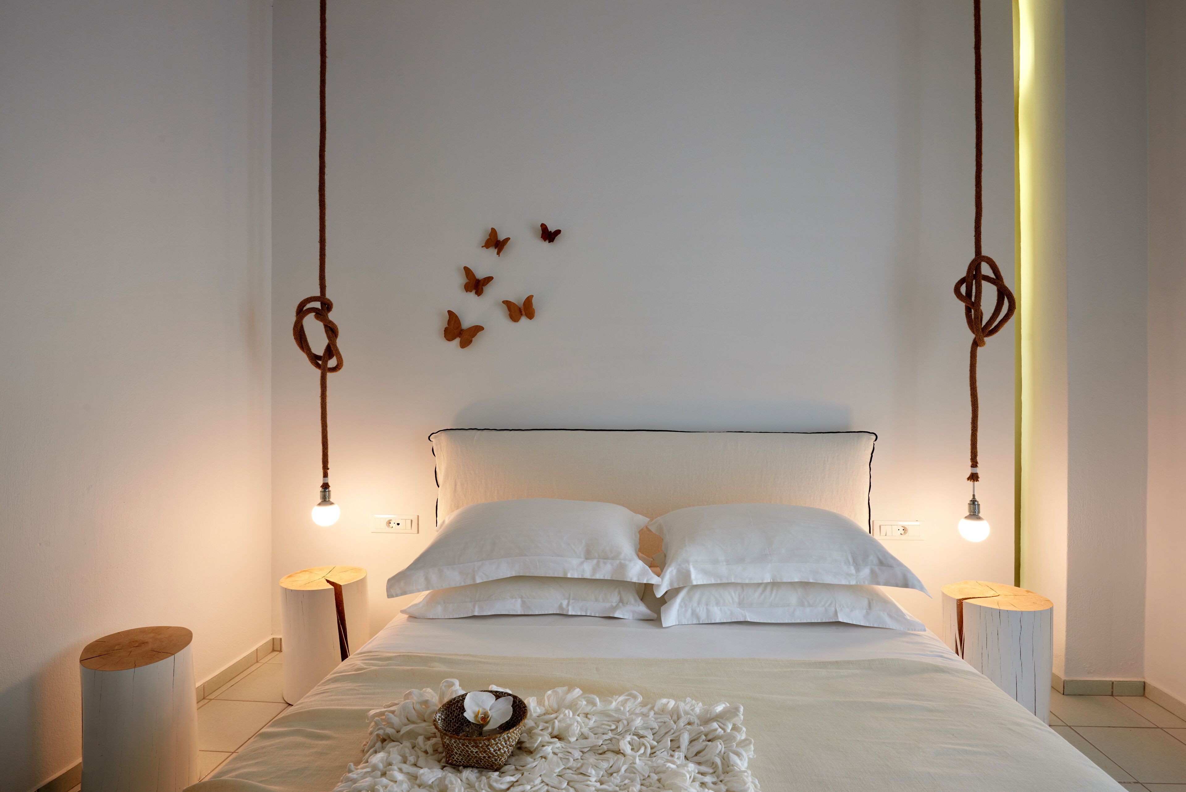 A bedroom with a bed, white pillows, a bedside table, a wall-mounted light fixture, and a small wall decoration.