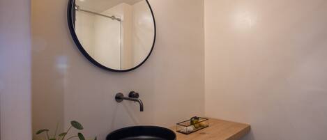 A modern bathroom with a round mirror, a black sink, a wooden countertop, and a potted plant.