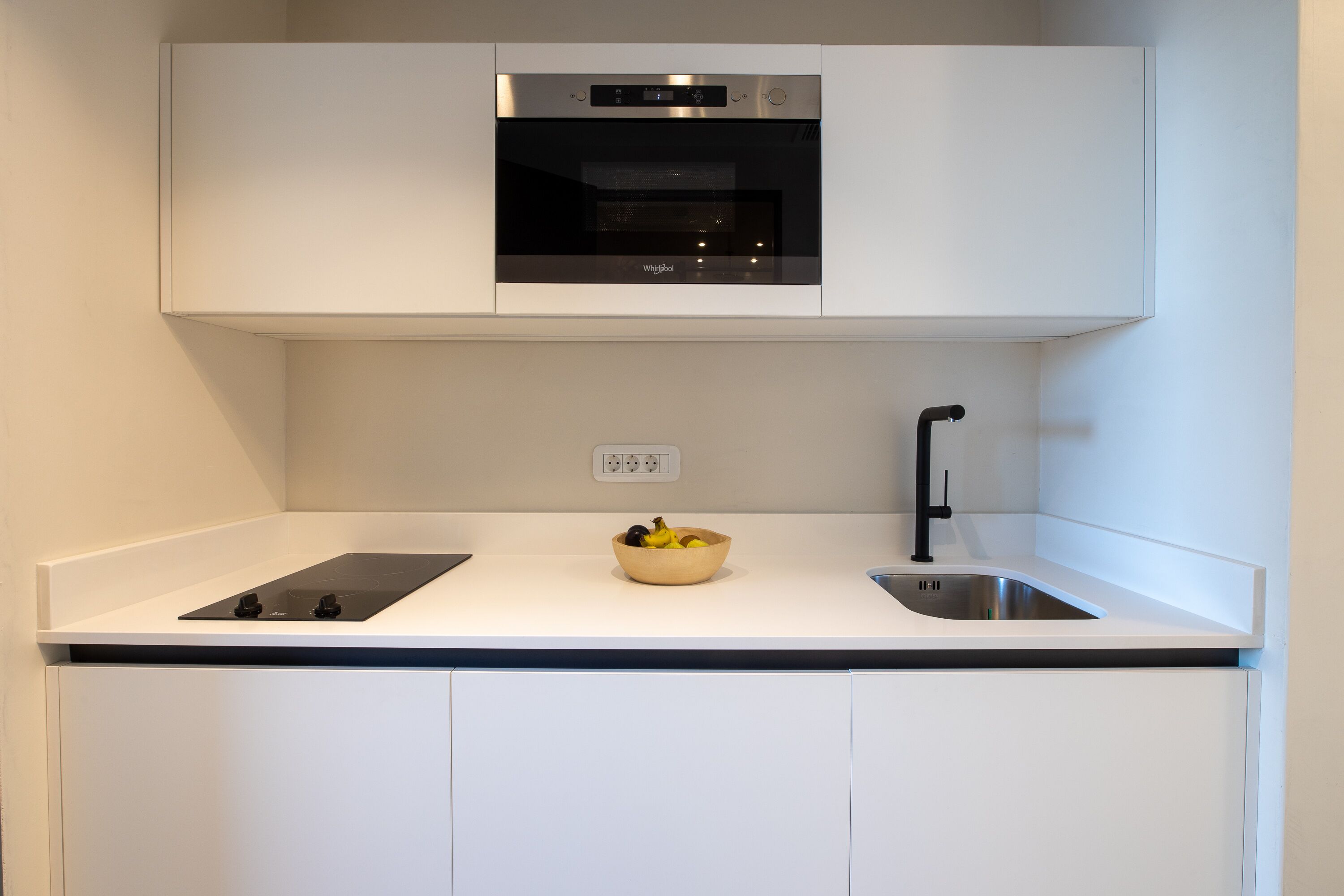 A modern kitchen with a built-in oven, a sink, and a countertop with a bowl of fruit.