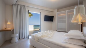 A modern bedroom with a large bed, a TV on the wall, and a view of the ocean through a sliding door. - Akrogiali Beach Hotel Apartments (Hersonissos)