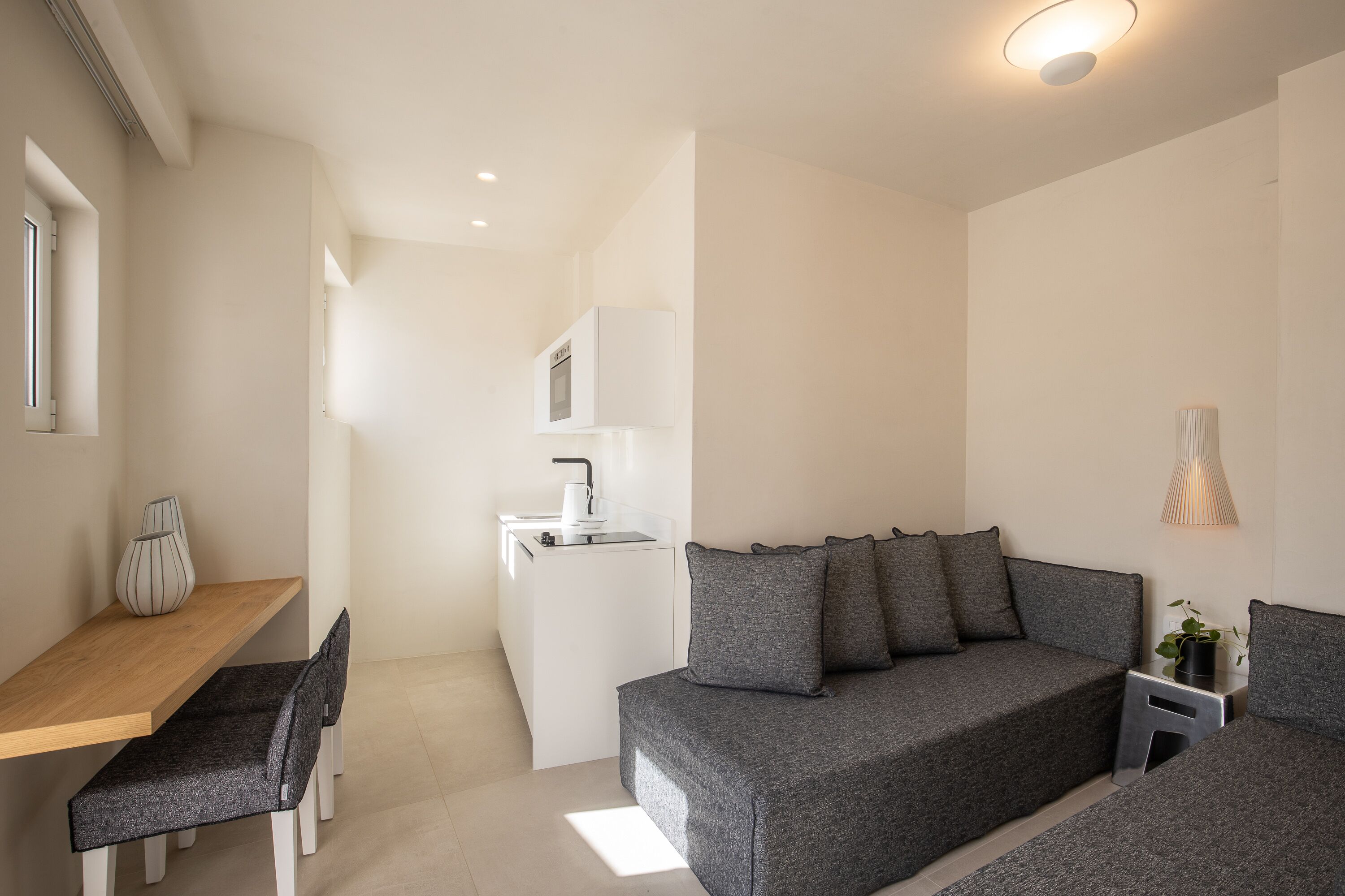 Et moderne, minimalistisk værelse med en grå sofa, et træspisebord og et hvidt tekøkken.