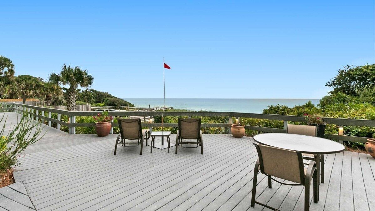 A wooden deck with outdoor seating, overlooking a beach and ocean.