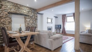 A dining area with a stone wall, wooden table, and leather chairs. There is a sofa and a television in the background.